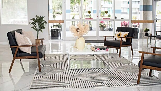 A modern lobby with two black leather sofas, a geometric patterned rug, and a large glass door leading outside. - Palm Tree Inn Altamonte Springs Orlando (Altamonte Springs)