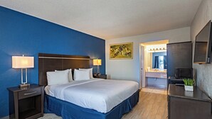 A hotel room with a large bed, two bedside tables with lamps, a flat-screen TV, a small plant, and a bathroom visible through an open door. - Palm Tree Inn Altamonte Springs Orlando (Altamonte Springs)