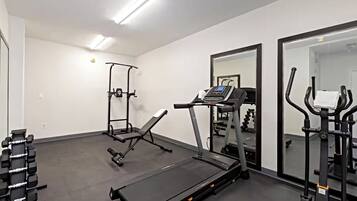 A gym with a treadmill, weight bench, and dumbbells.