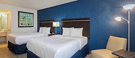 Camera d'albergo con due letti, una sedia, un tavolo e un comodino.