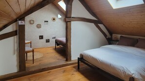 Um quarto de sótão acolhedor, com teto inclinado, vigas de madeira, uma cama, uma cadeira e uma pequena mesa.