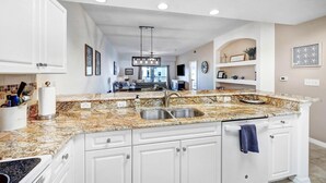 A kitchen with white cabinets, granite countertops, a double sink, and a hanging light fixture. - Oceanwalk 8-504 - A 3 bed 2 bath Seabreeze escape (New Smyrna Beach)