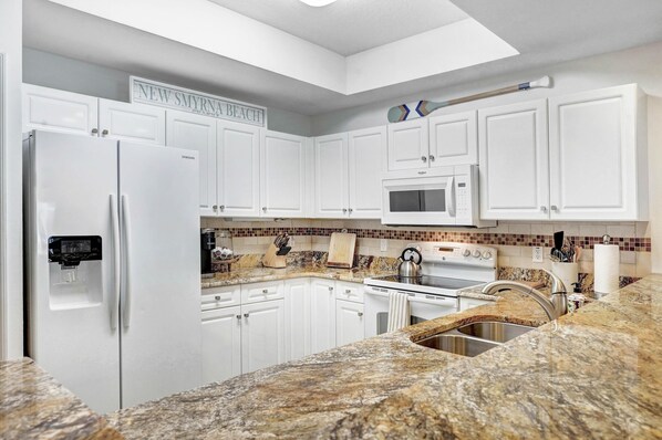 A kitchen with white cabinets, a refrigerator, a microwave, a stove, and granite countertops.