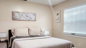 A bedroom with a bed, a nightstand, a lamp, and a window with blinds. - Toria Suites 920 (Lakeland)