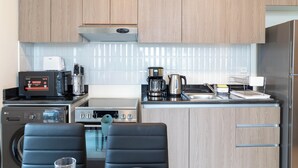 A compact kitchen with wooden cabinets, a microwave, a coffee maker, a kettle, and a dishwasher. - Bloomfields Artistic STU in The View (Abu Dhabi)