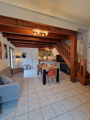 A spacious living area with a wooden ceiling, a dining table with chairs, a sofa, and a kitchen in the background.