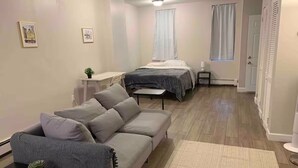 Un espacio habitable compacto con sofá, cama, una mesita y una ventana con cortinas.