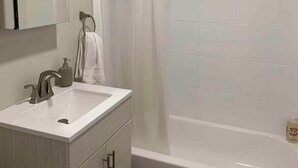 Un baño moderno con lavamanos, espejo y bañera blancos.