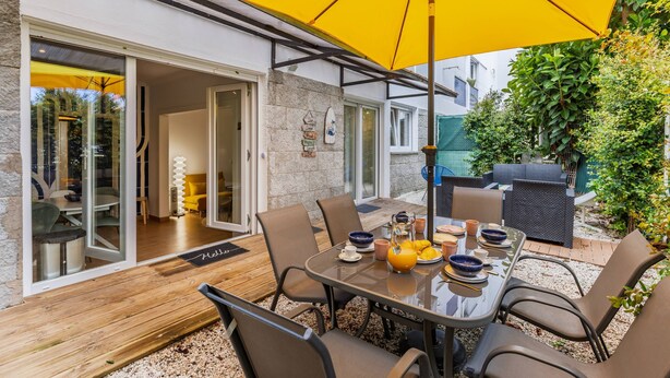 Een buiten eethoek met een tafel voor vier personen, omringd door stoelen, onder een grote gele parasol.