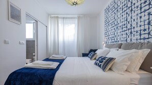Een hotelkamer met een bed, witte gordijnen, een patroonwand en een plafondlamp.