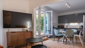 Een moderne woonkamer met een flatscreentelevisie, een houten kast en een eethoek met een tafel en stoelen.