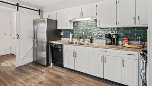 Una cocina moderna con armarios blancos, un refrigerador de acero inoxidable, lavavajillas y una encimera de granito.