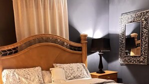Un dormitori amb un llit de fusta, una taula de nit, una làmpada i un mirall.