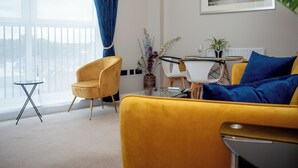 A modern living room with a yellow sofa, a small round table, and a dining area with a white table and chairs.