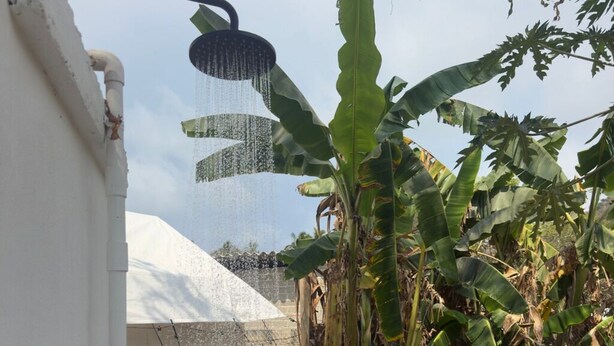A showerhead with water spray, a white wall, and banana plants. - Glamping in Quimixto 5 minutes from the beach (Quimixto)