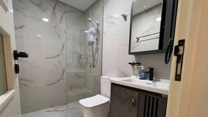Et moderne badeværelse med brusekabine i glas, hvidt toilet og marmorfliser.