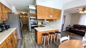A modern kitchen with wooden cabinets, a central island with stools, and a dining area with a table and chairs. - Granny's at the Beach…Heated Pool (Panama City Beach)