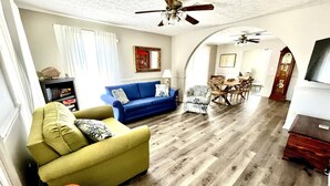A living room with a blue sofa, a yellow armchair, and a wooden coffee table. There is a dining area with a table and chairs in the background. - Granny's at the Beach…Heated Pool (Panama City Beach)