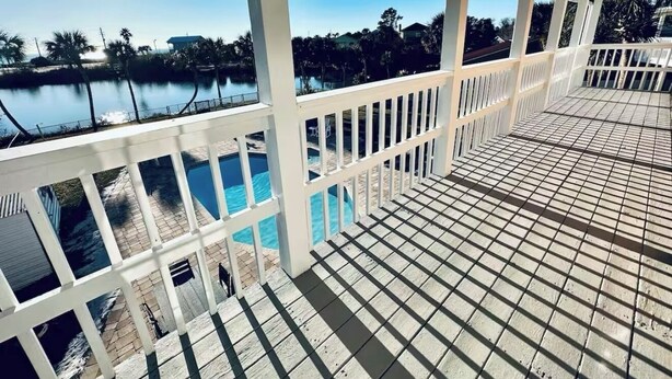 A covered outdoor deck with a view of a swimming pool and a body of water. - Granny's at the Beach…Heated Pool (Panama City Beach)