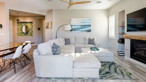 A modern living room with a sectional sofa, a dining area, a fireplace, and a large TV. - Two Resort Style Homes Steps from Each Other, 7 Bedrooms, Pool, Hot Tub, Misters (Cathedral city)