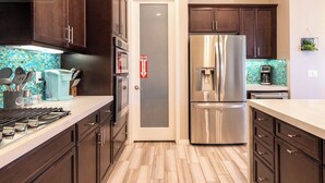 A modern kitchen with dark wood cabinets, stainless steel appliances, a tiled backsplash, and a door with a fire exit sign. - Two Resort Style Homes Steps from Each Other, 7 Bedrooms, Pool, Hot Tub, Misters (Cathedral city)