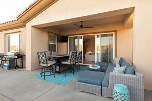 Une terrasse extérieure aménagée avec un canapé, une table à manger, des chaises et un ventilateur de plafond.