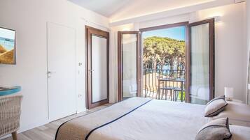 Habitación de hotel con una cama grande, vista a un balcón con mobiliario exterior y una puerta que conduce a un espacio privado.