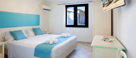 A hotel room with a bed, a desk, a chair, a window, and a wall-mounted TV.