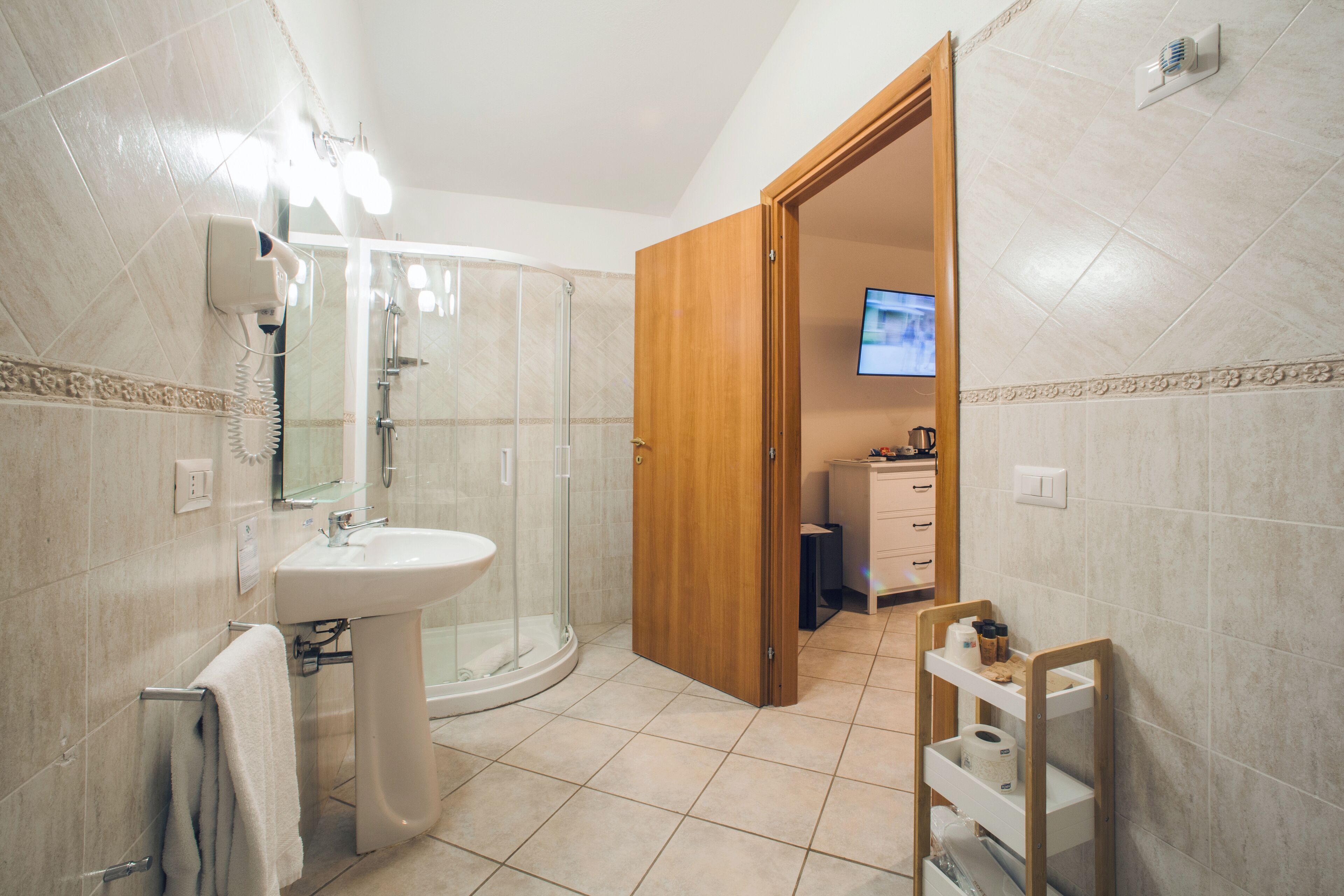 Un baño con lavamanos, cabina de ducha de vidrio y puerta de madera que da a una habitación con televisión.