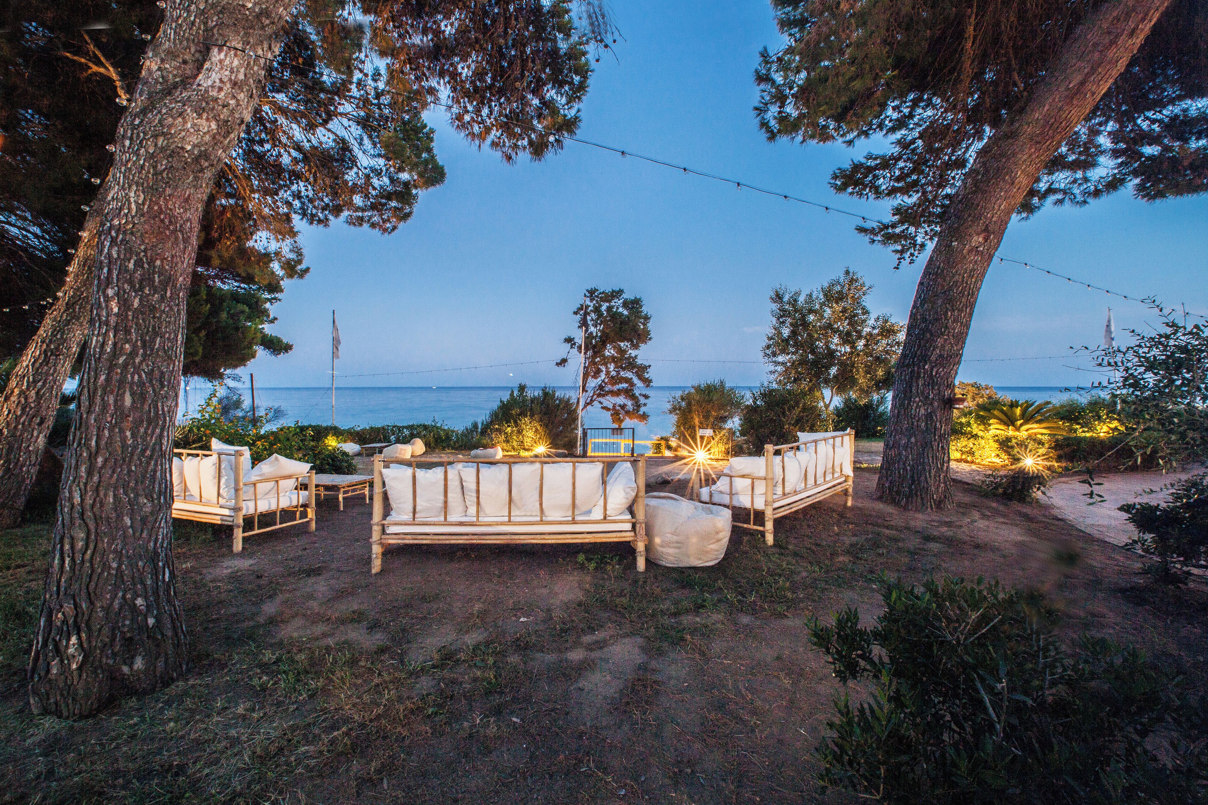 An outdoor seating area with wooden furniture and string lights, overlooking a body of water.