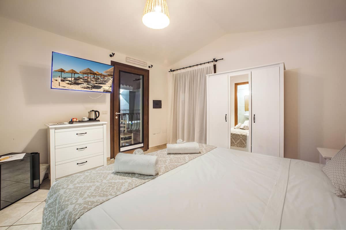 A hotel room with a bed, a desk, a chair, a wardrobe, and a bathroom visible through a glass door.