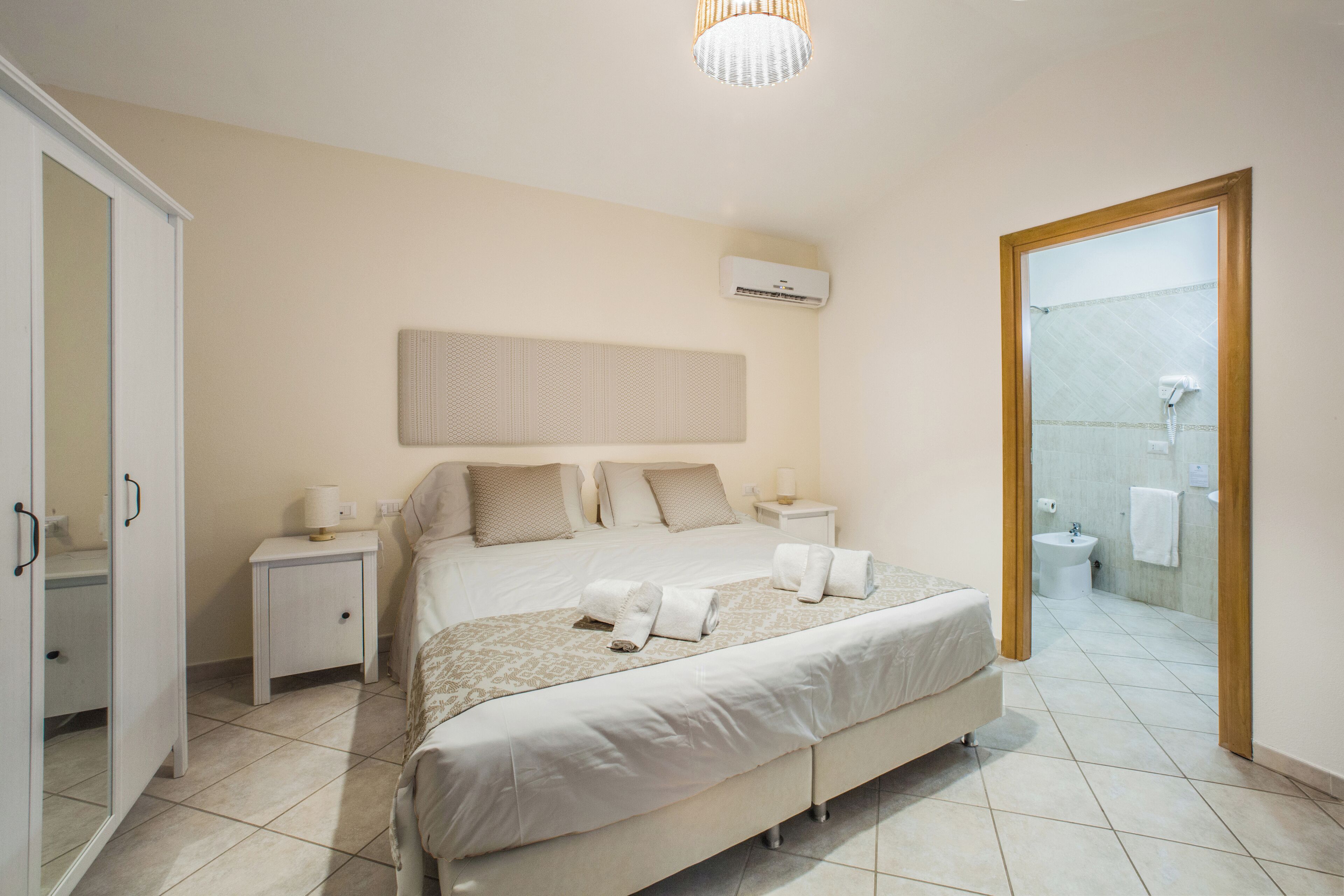 A bedroom with a large bed, bedside tables, a wardrobe, and a bathroom visible through an open door.