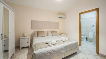 A bedroom with a large bed, bedside tables, a wardrobe, and a bathroom visible through an open door.