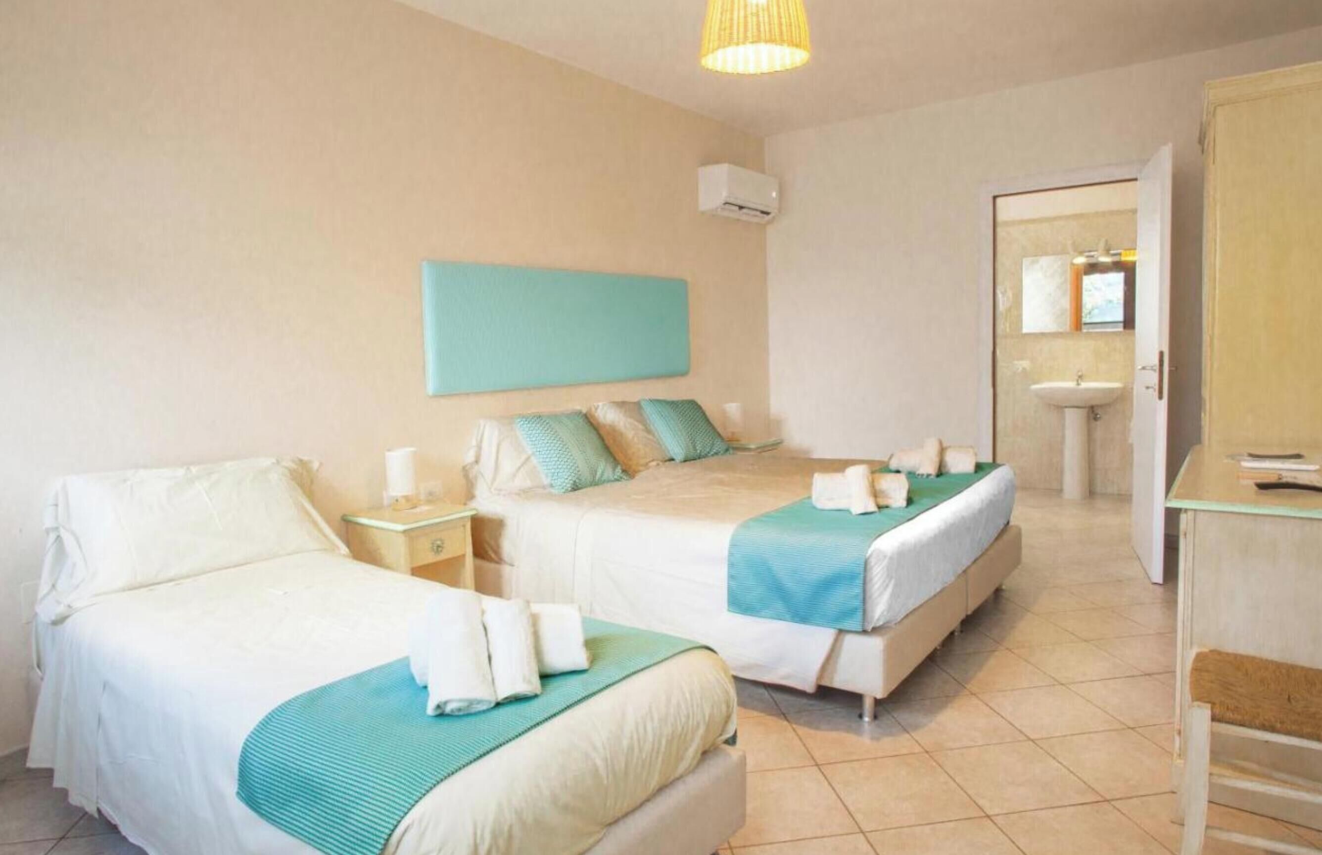 Hotelkamer met twee bedden, een nachtkastje met lamp, een wandairconditioner en een badkamer met wastafel en spiegel.