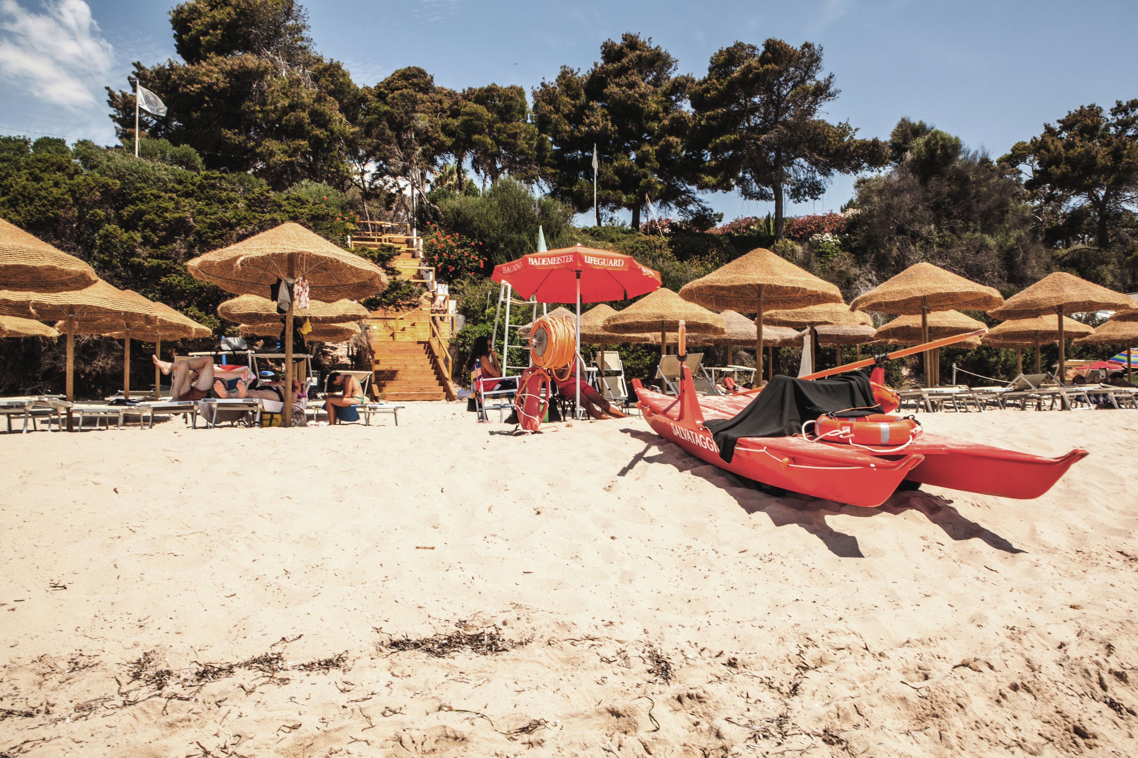 Ein Strand mit Reetsonnenstühlen, Liegestühlen und einem roten Boot.