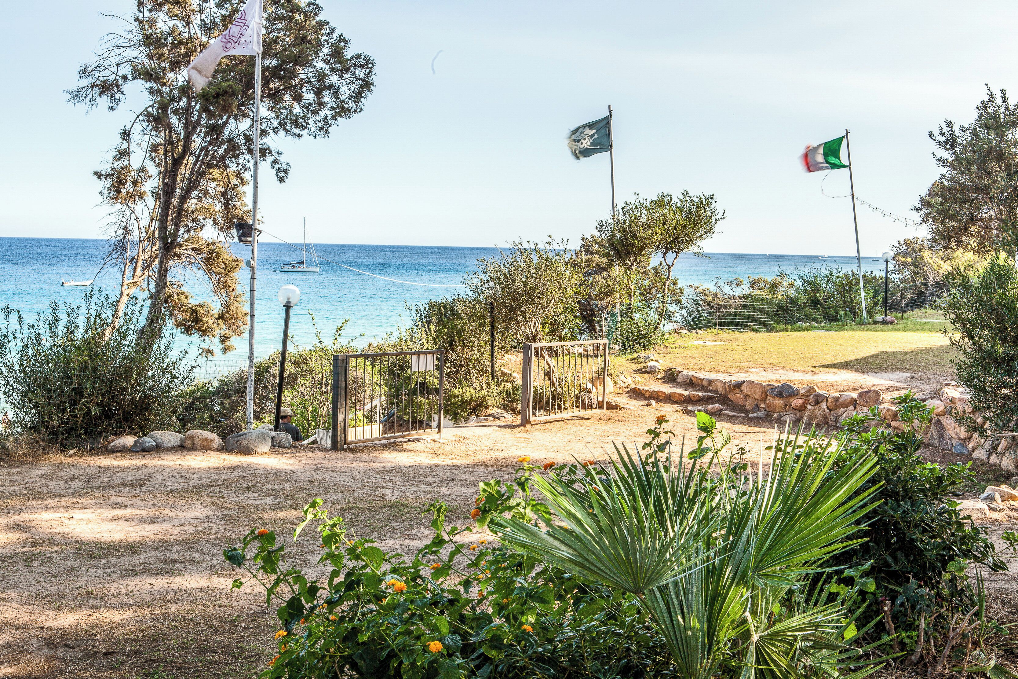 Un jardin situé sur la côte, avec une porte, des drapeaux et une vue sur la mer.
