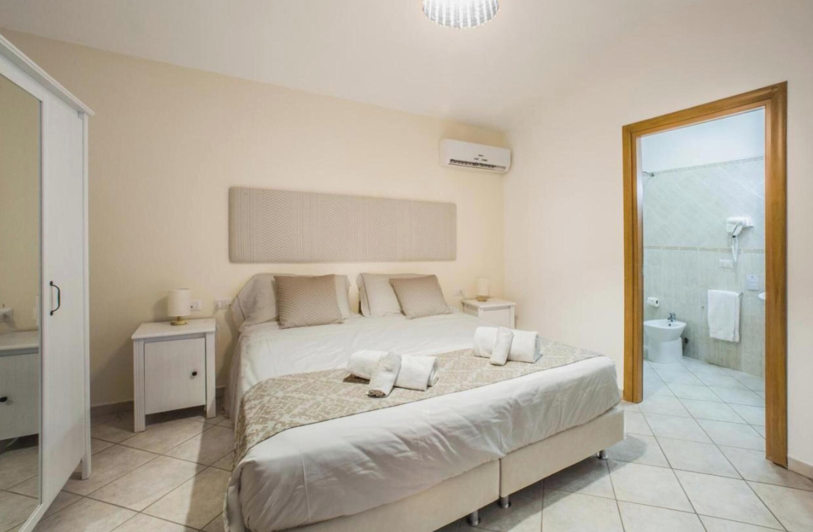 Una camera da letto con un letto, comodini, uno specchio, un condizionatore d'aria a parete e un bagno con doccia.