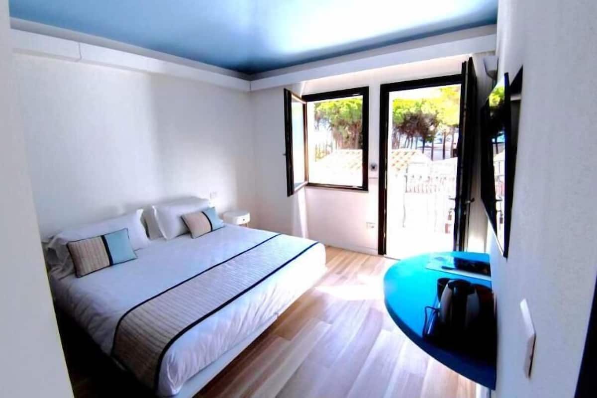 A bedroom with a bed, a nightstand, a window, and a door leading to an outdoor area.