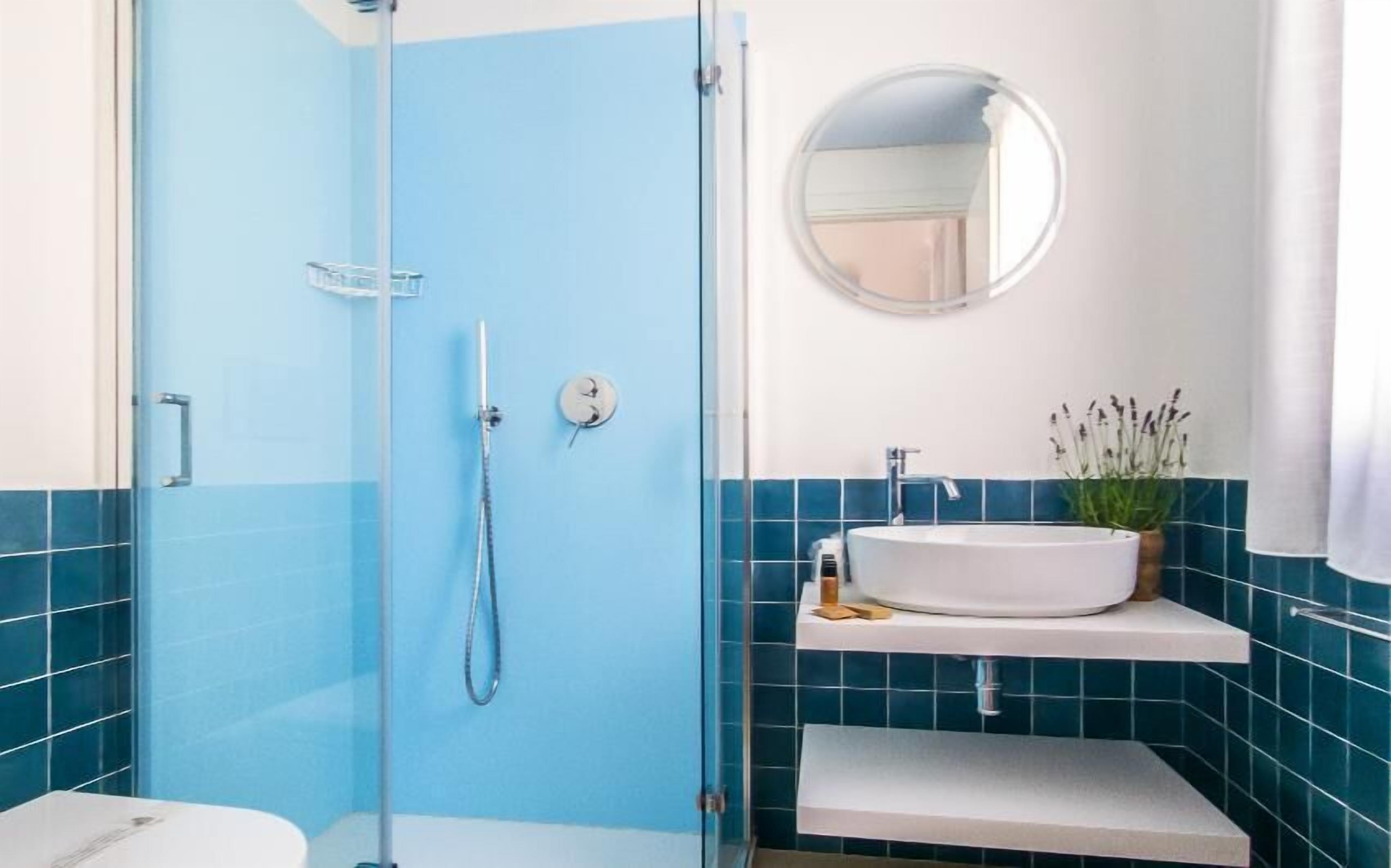 Ein Badezimmer mit einer Duschkabine, einem weißen Waschbecken mit Spiegel darüber und blauen Fliesenwänden.