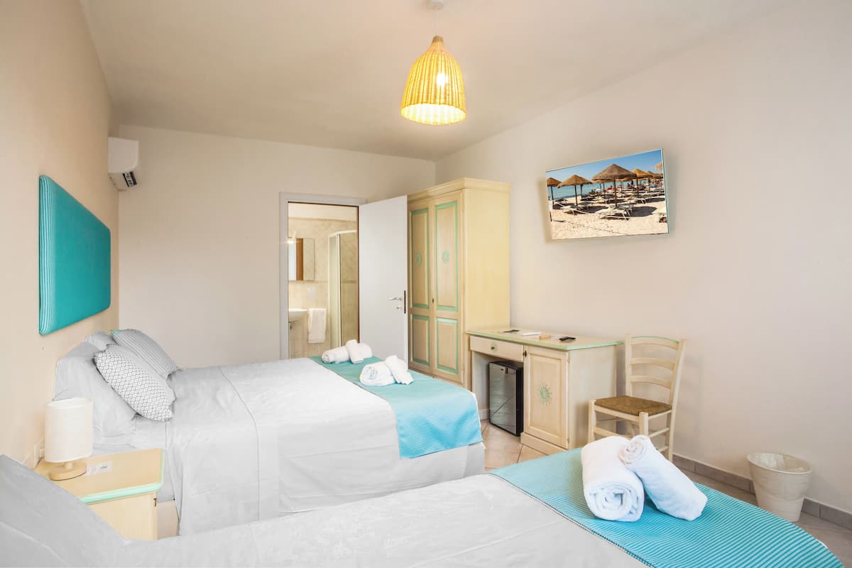 A hotel room with two beds, a desk, a chair, a trash bin, and a painting on the wall.