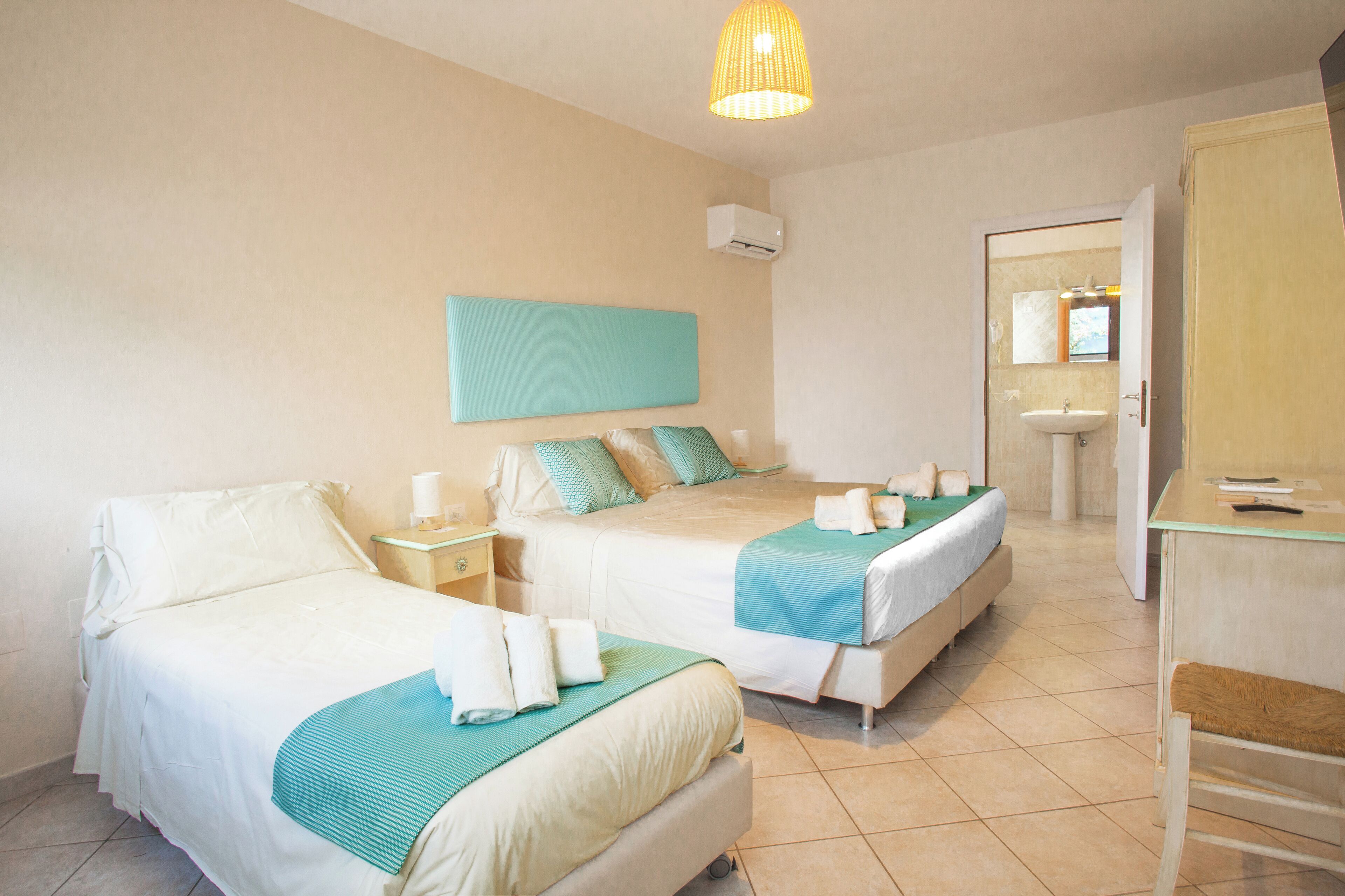 A hotel room with two beds, a bedside table, a mirror, a sink, and a wardrobe.