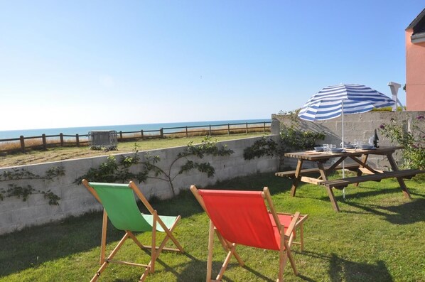 A patio with a view of the sea, a picnic table, and two colorful chairs.