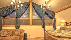 A bedroom with a bed, a sofa, a chandelier, and a window with curtains.