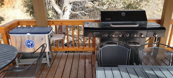 Una terraza de madera con una parrilla, un enfriador y asientos para exteriores.