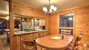 A wooden interior with a round dining table, chairs, a kitchen area, and a window.