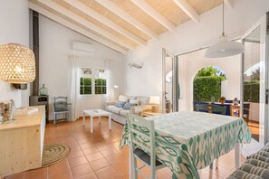 Amplia sala de estar con una mesa de comedor, sofá y vistas a un jardín exuberante a través de un ventanal abierto.
