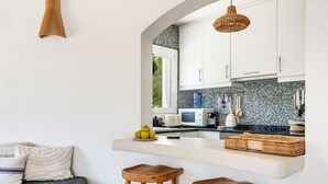 A modern kitchen with white cabinets, a black tiled backsplash, and a wooden bar counter. - Villa Fontana, little paradise (Punta Prima)