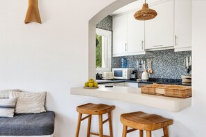 A modern kitchen with white cabinets, a black tiled backsplash, and a wooden bar counter.