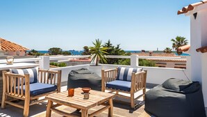 A rooftop terrace with wooden furniture, a table, and a view of the sea and buildings. - Villa Fontana, little paradise (Punta Prima)