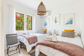 A bedroom with two beds, a chair, and artwork on the walls.